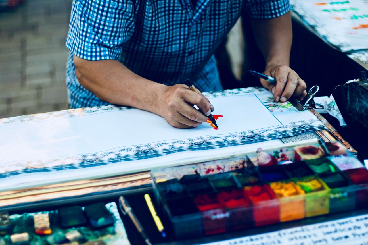 Artist working on a colorful traditional painting using vibrant inks and brushes.