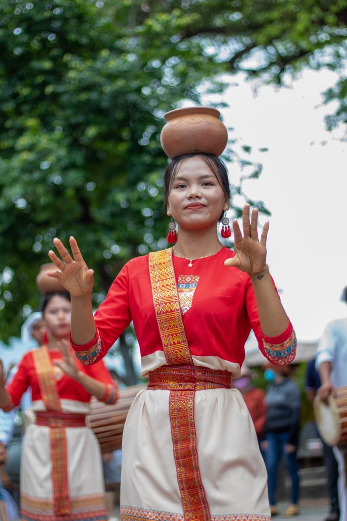 Women in vibrant attire performing a traditional Asian dance outdoor with clay pots balancing on their heads.