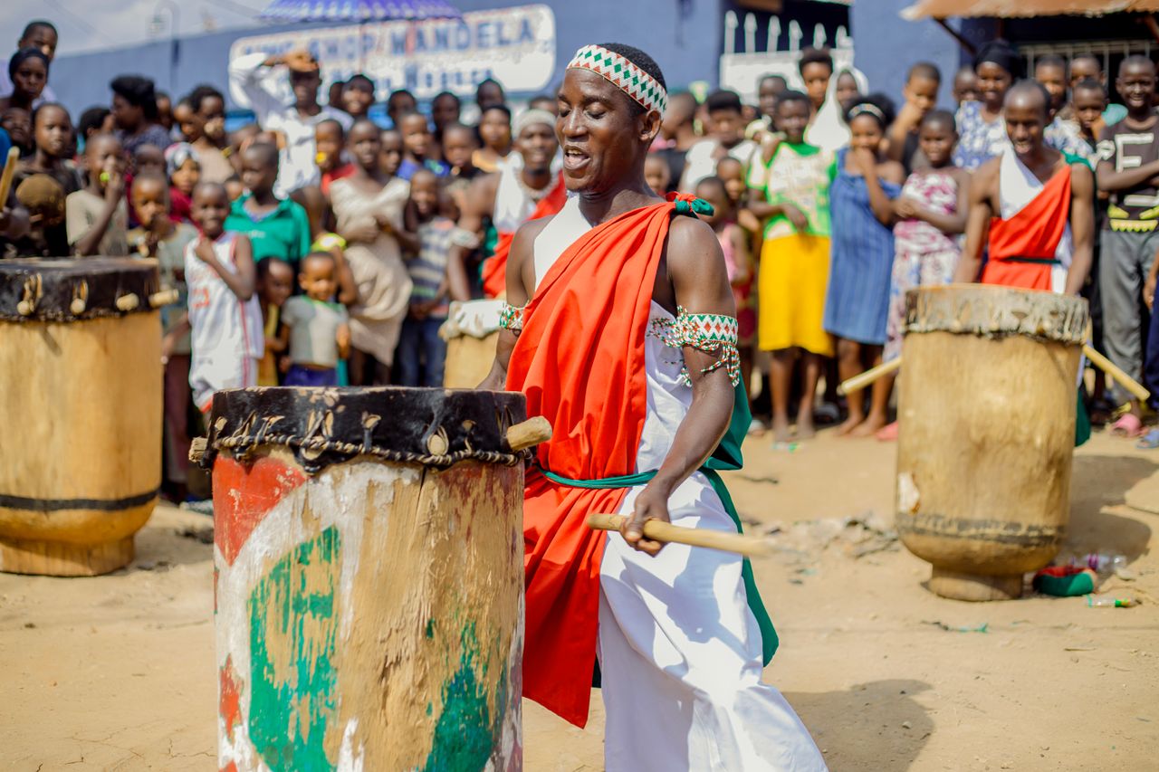 Traditional African drumming performance with vibrant cultural attire, engaging an excited crowd outdoors.