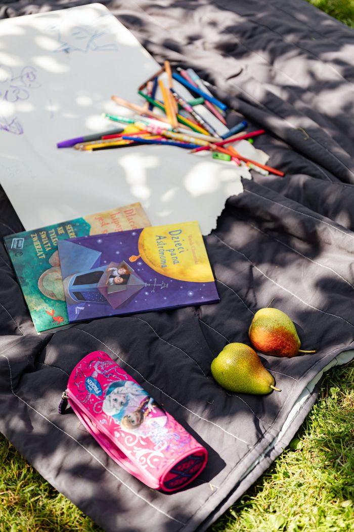 Art supplies and books on a blanket in the sunlit garden.