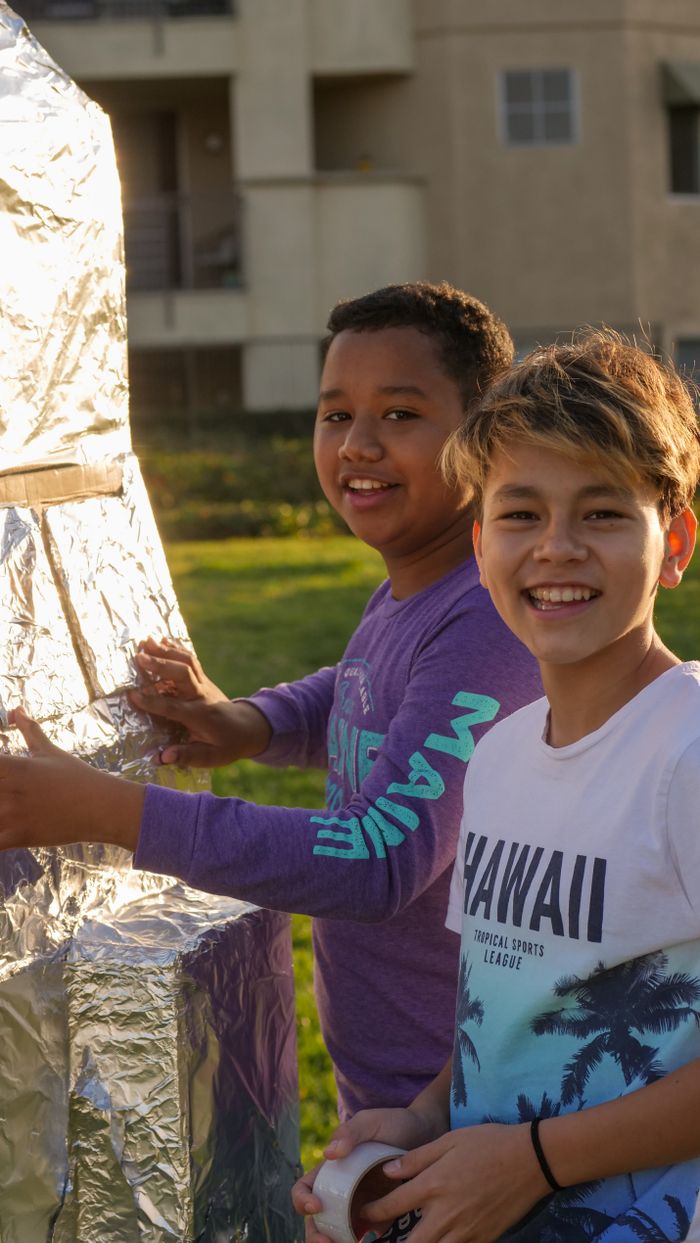 Two boys playing with a homemade rocket outdoors, enjoying a sunny day.
